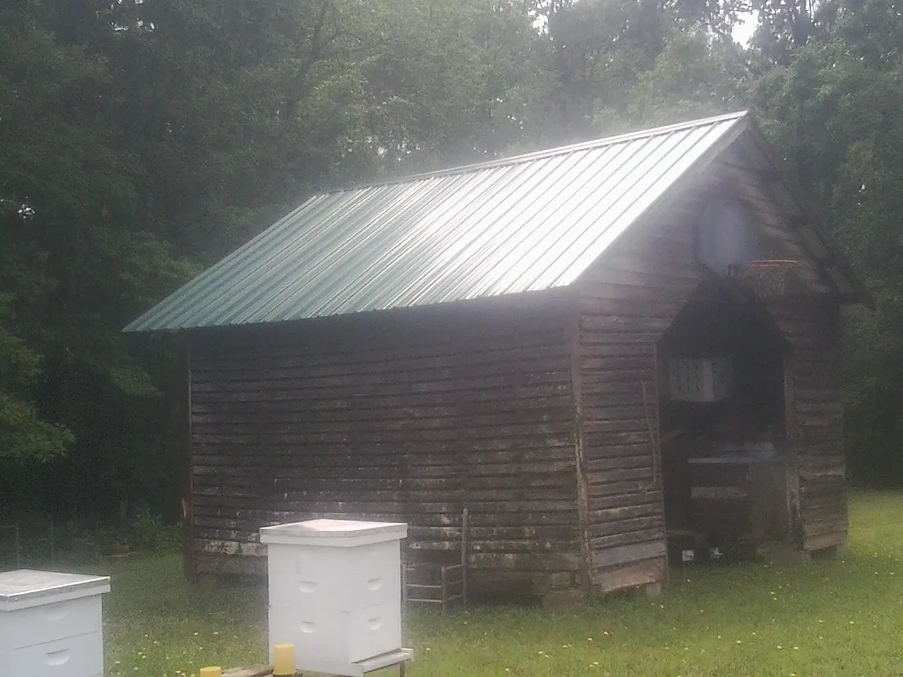 Green metal roof on a weathered barn beside stacked beehives in Lakeville
